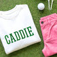 White sweatshirt with 3d embroidered 'CADDIE' design in kelly green thread, paired with pink shorts, a golf ball and golf tees