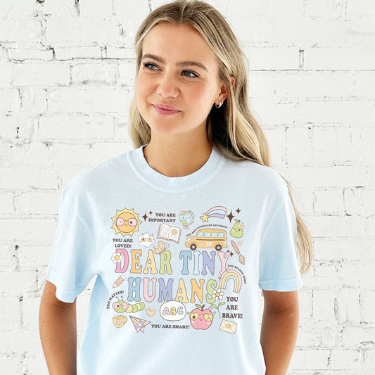 woman wearing a small chambray comfort colors t-shirt with a colorful fun school icon dear tiny humans printed design on the front