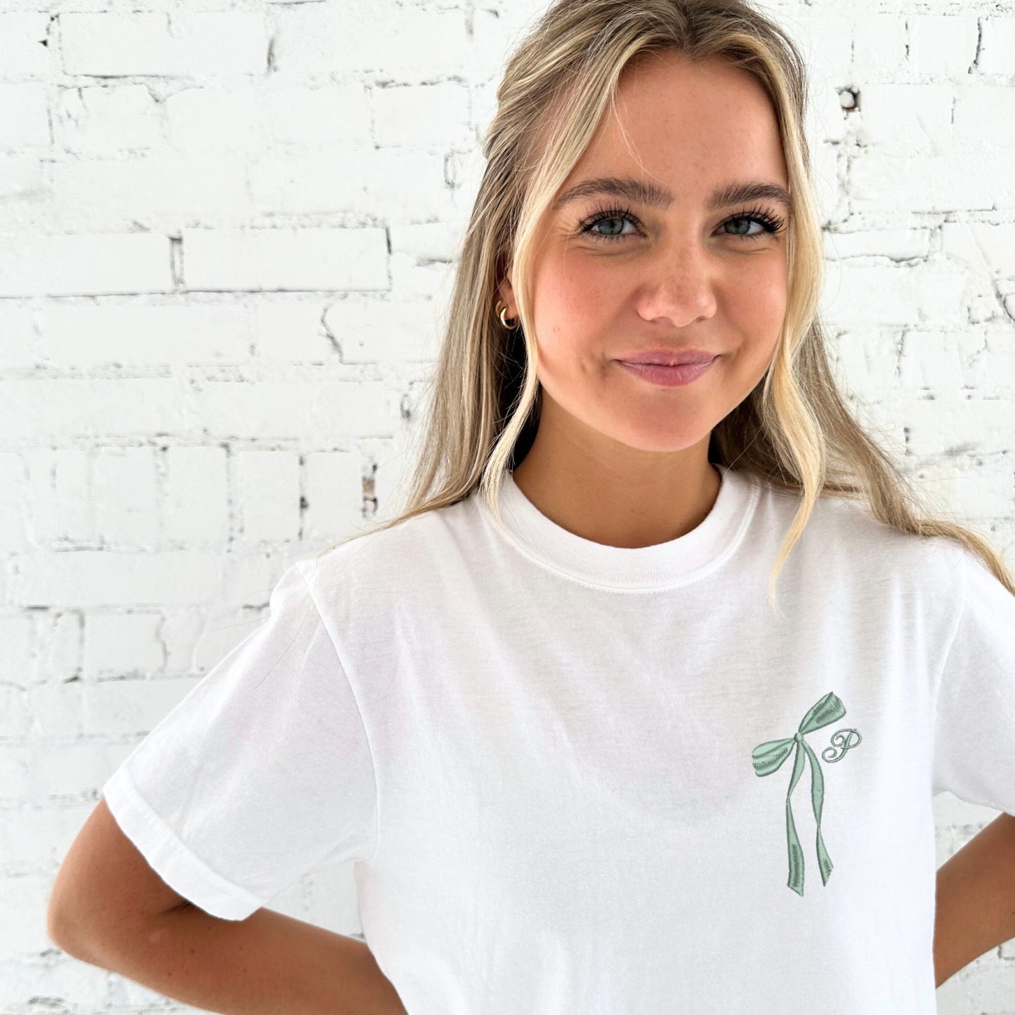 white comfort colors t-shirt with embroidered ribbon bow and cursive initial embroidered on the left chest in eucalyptus thread