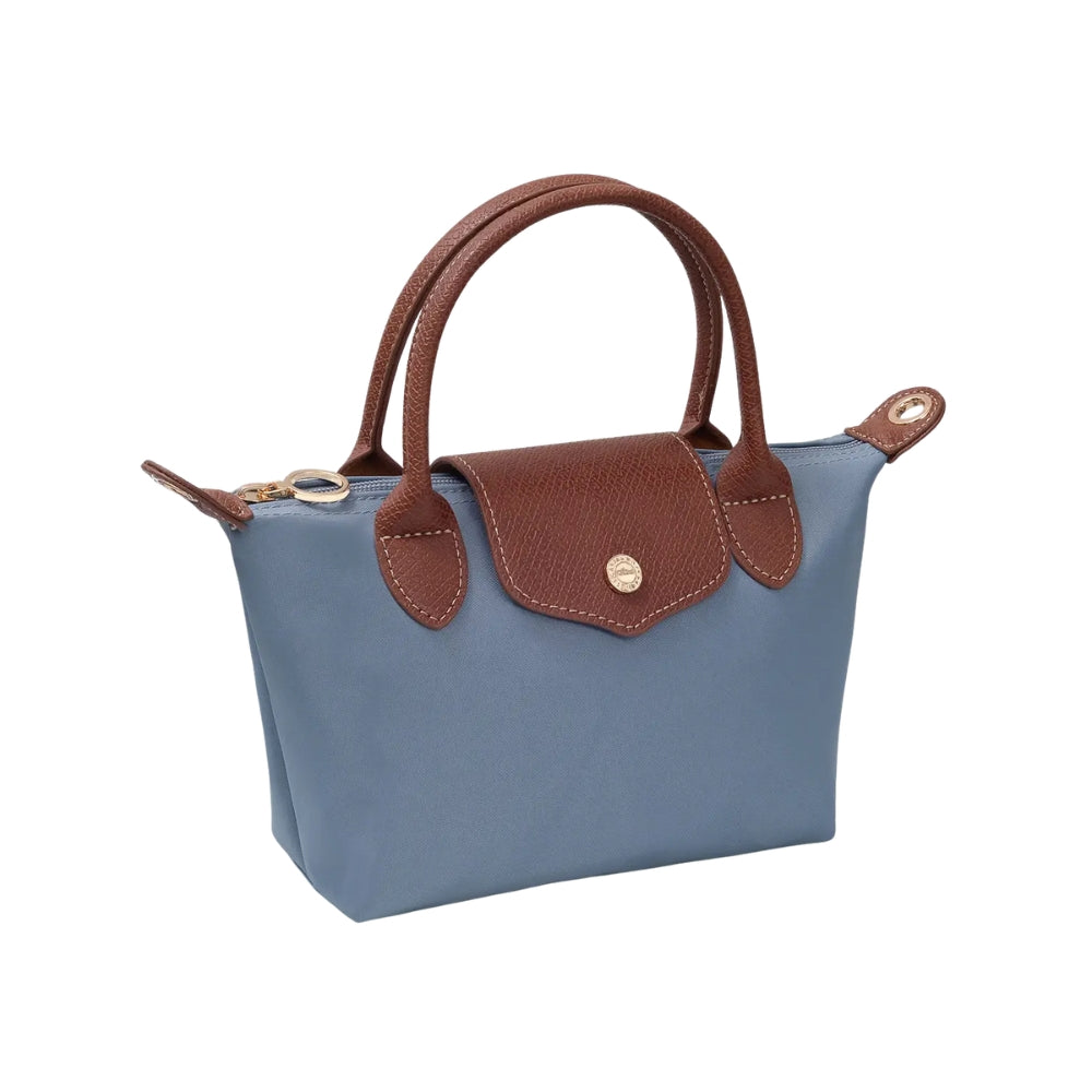 A small blue canvas handbag with brown leather handles, trim, and a front flap closure, shown on a plain white background.
