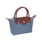 A small blue canvas handbag with brown leather handles, trim, and a front flap closure, shown on a plain white background.