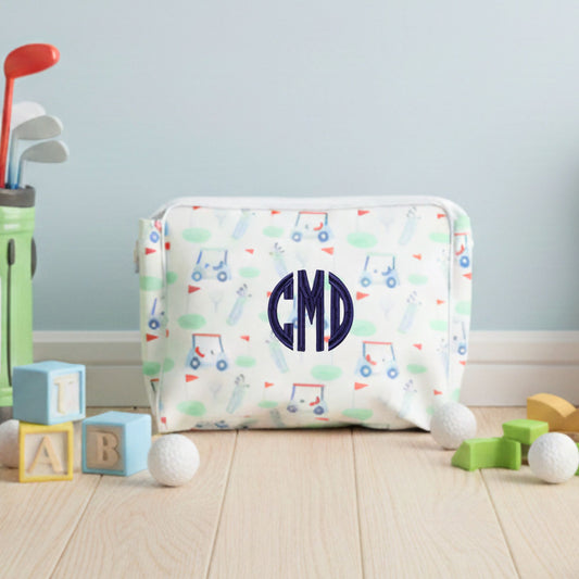 Children's pouch with golf pattern and 'CMD' monogram, surrounded by toys on a wooden floor.