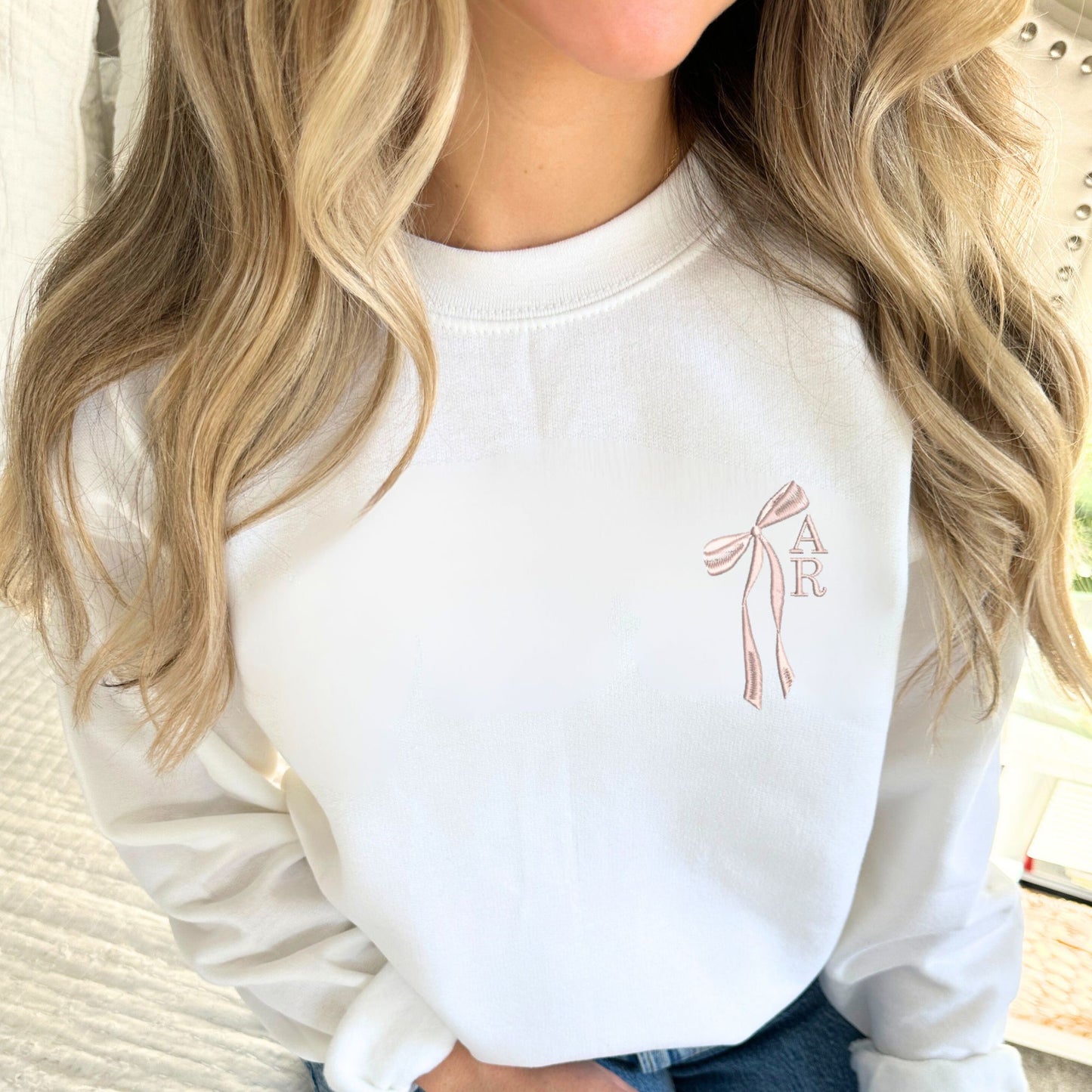 girl wearing a white crewneck sweatshirt with custom ribbon bow and stacked initials embroidered on the left chest with powder pink thread