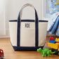 canvas tote bag with navy accents and 'RDE' initials on a wooden floor with toys around