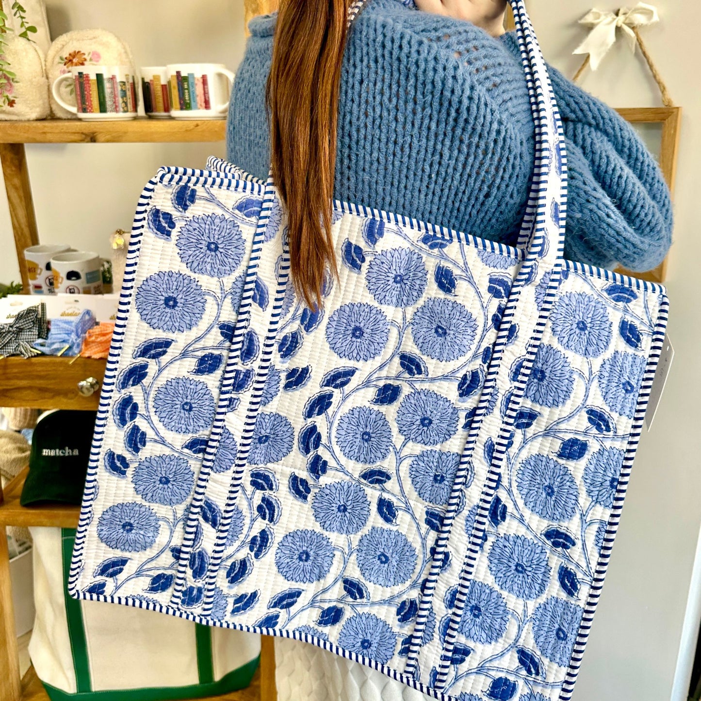 Person holding a blue floral patterned tote bag in a casual setting.