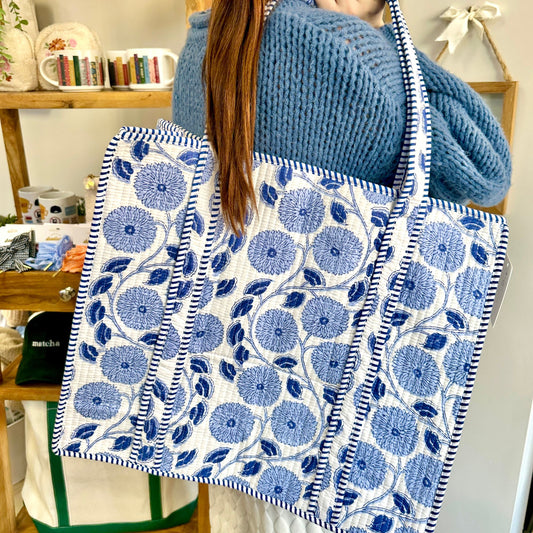 Person holding a blue floral patterned tote bag in a casual setting.