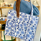 Person holding a blue floral patterned tote bag in a casual setting.