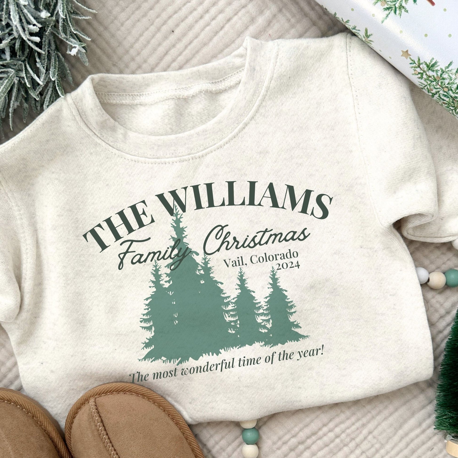 natural heather youth sweatshirt with a custom Christmas print featuring a family name, vacation location, year, trees, and a "The most wonderful time of the year!" quote in green ink