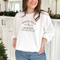 young woman wearing a sweet cream crewneck sweatshirt with embroidered north pole bakery design in ivy green and brown threads.