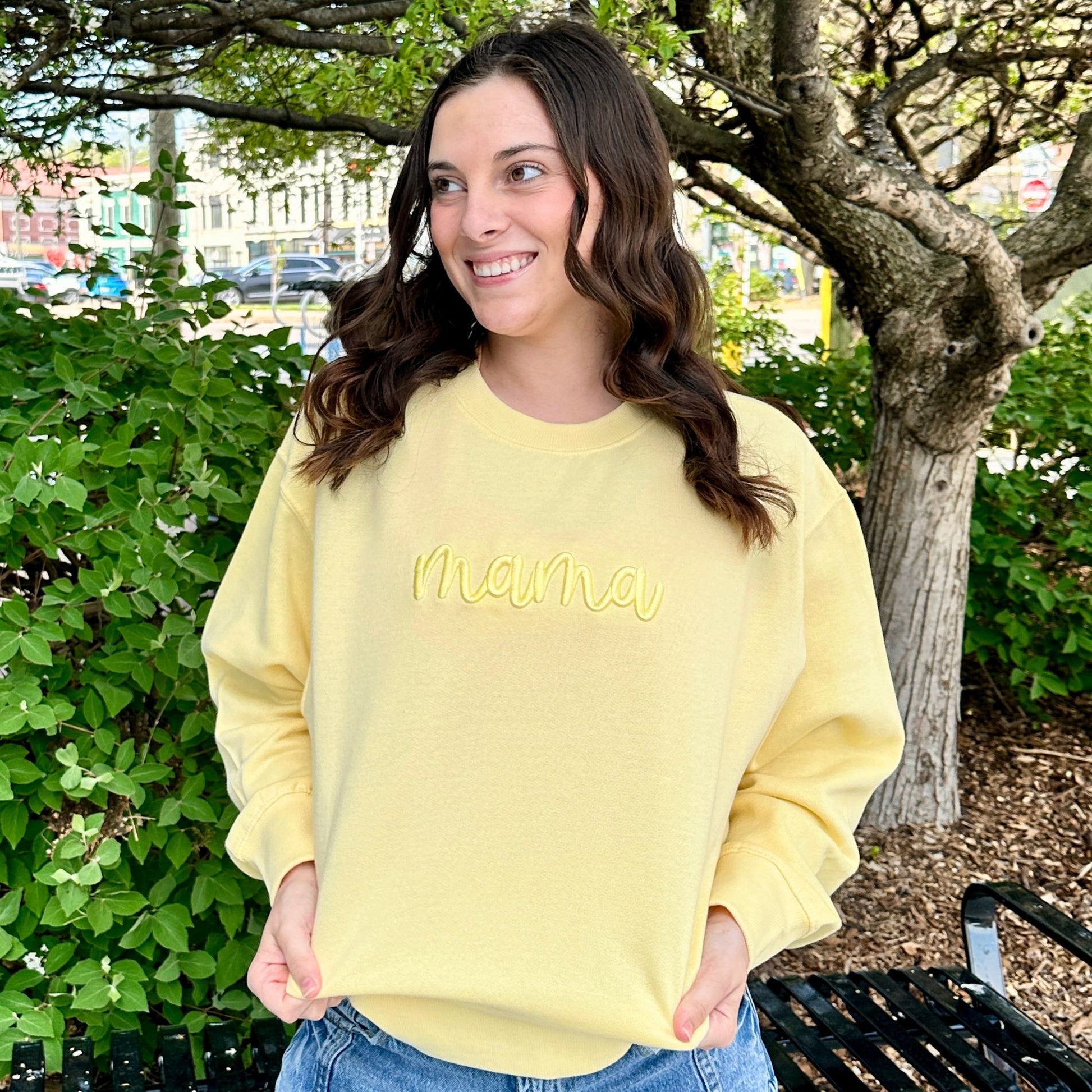 Woman wearing a yellow sweatshirt with 'mama' text outdoors.