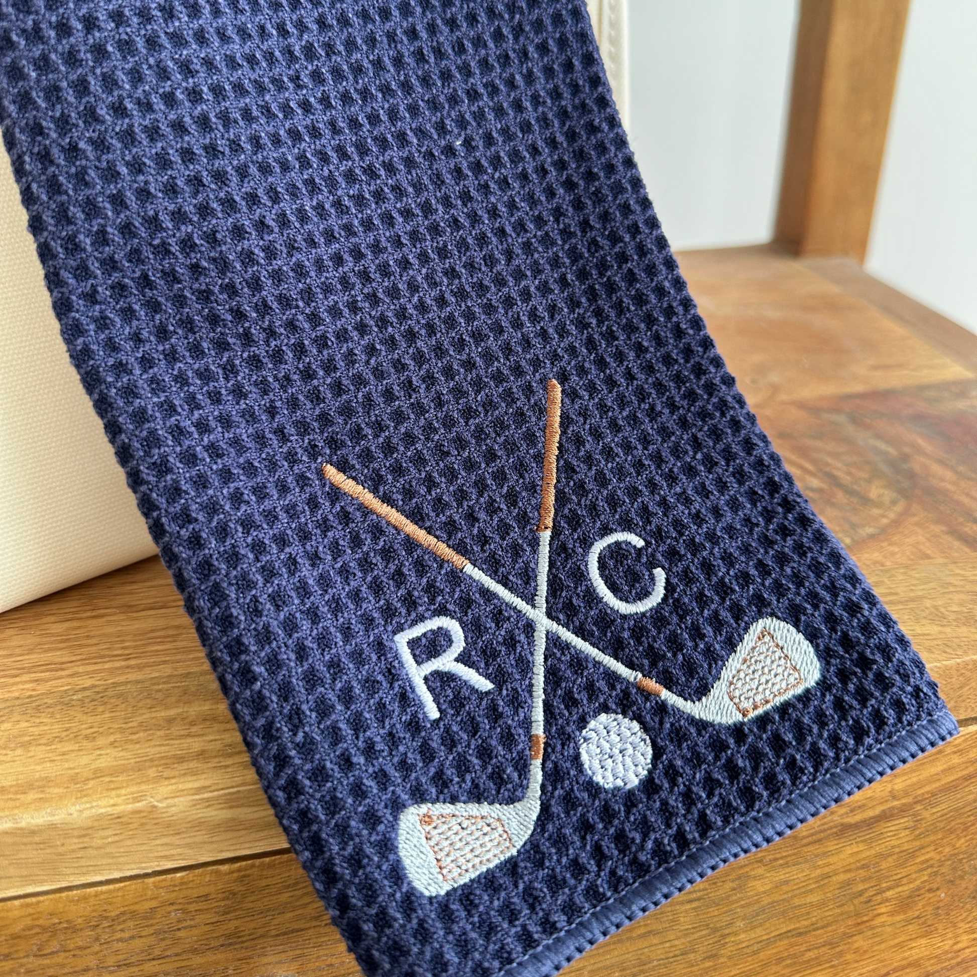 navy tri-fold waffle microfiber golf towel with carabiner and custom golf club and Arial font initials in white thread embroidered design