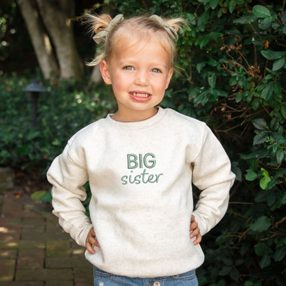 little girl wearing a Natural Heather toddler crewneck with custom BIG sister embroidered design on the center chest in eucalyptus thread