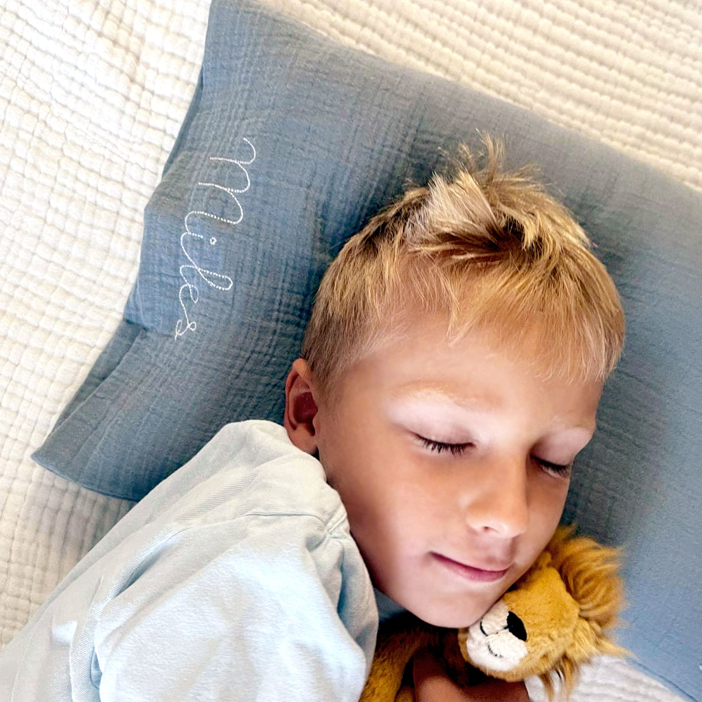 little boy laying on a custom pillow with a muslin pillowcase and personalized name stitched embroidery along the side