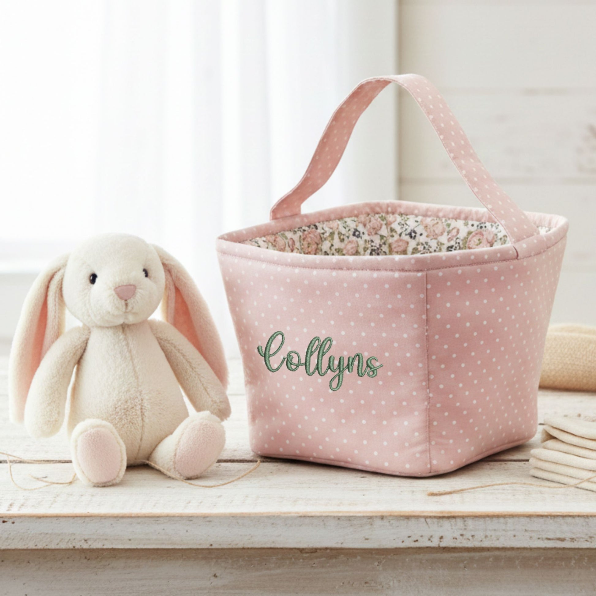 Pink polka dot storage basket with floral interior next to a plush bunny toy on a wooden surface.