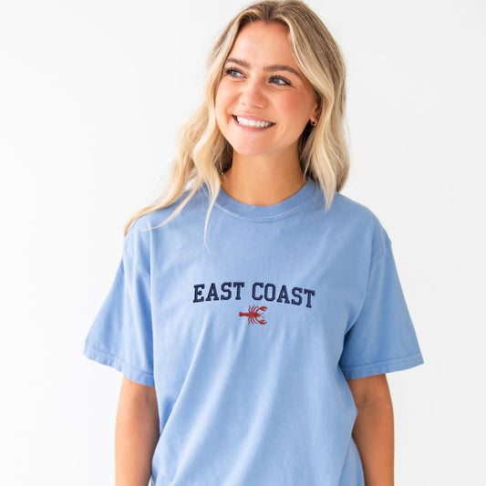 Woman wearing a light blue t-shirt with 'East Coast' and a lobster graphic on a white background