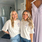 Two girls wearing white comfort colors t-shirts with custom ribbon bow and stacked initial embroidery on the left chest in smoky orchid thread.