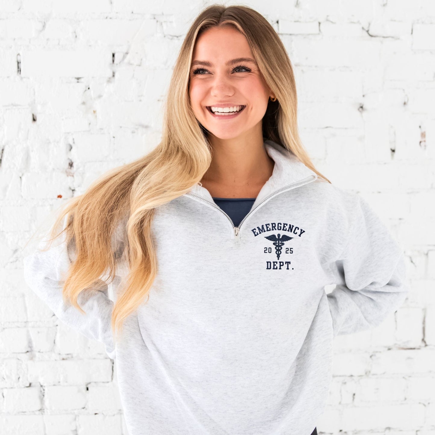 Girl wearing an ash quarter zip with custom embroidered registered nurse, date, and Caduceus symbol design on the left chest in navy thread