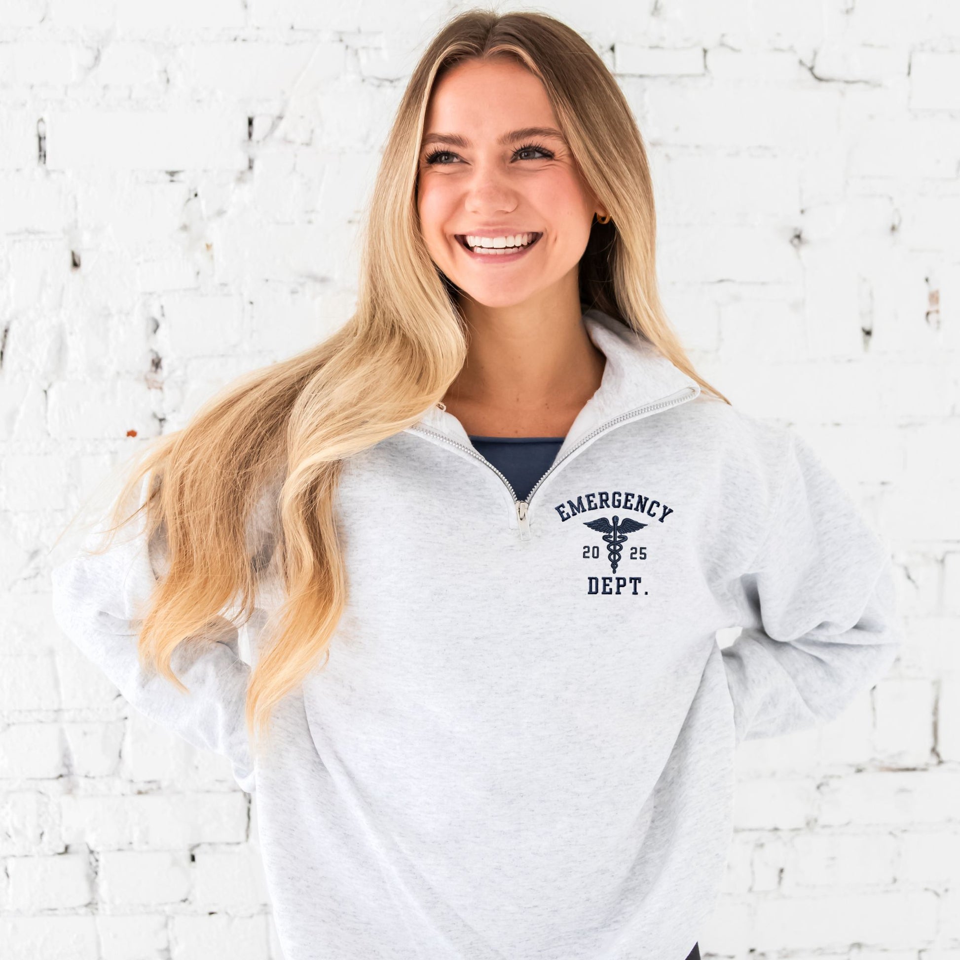 Girl wearing an ash quarter zip with custom embroidered registered nurse, date, and Caduceus symbol design on the left chest in navy thread