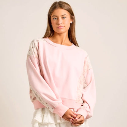 Woman wearing a pink sweater with floral patterned sleeves on a plain background