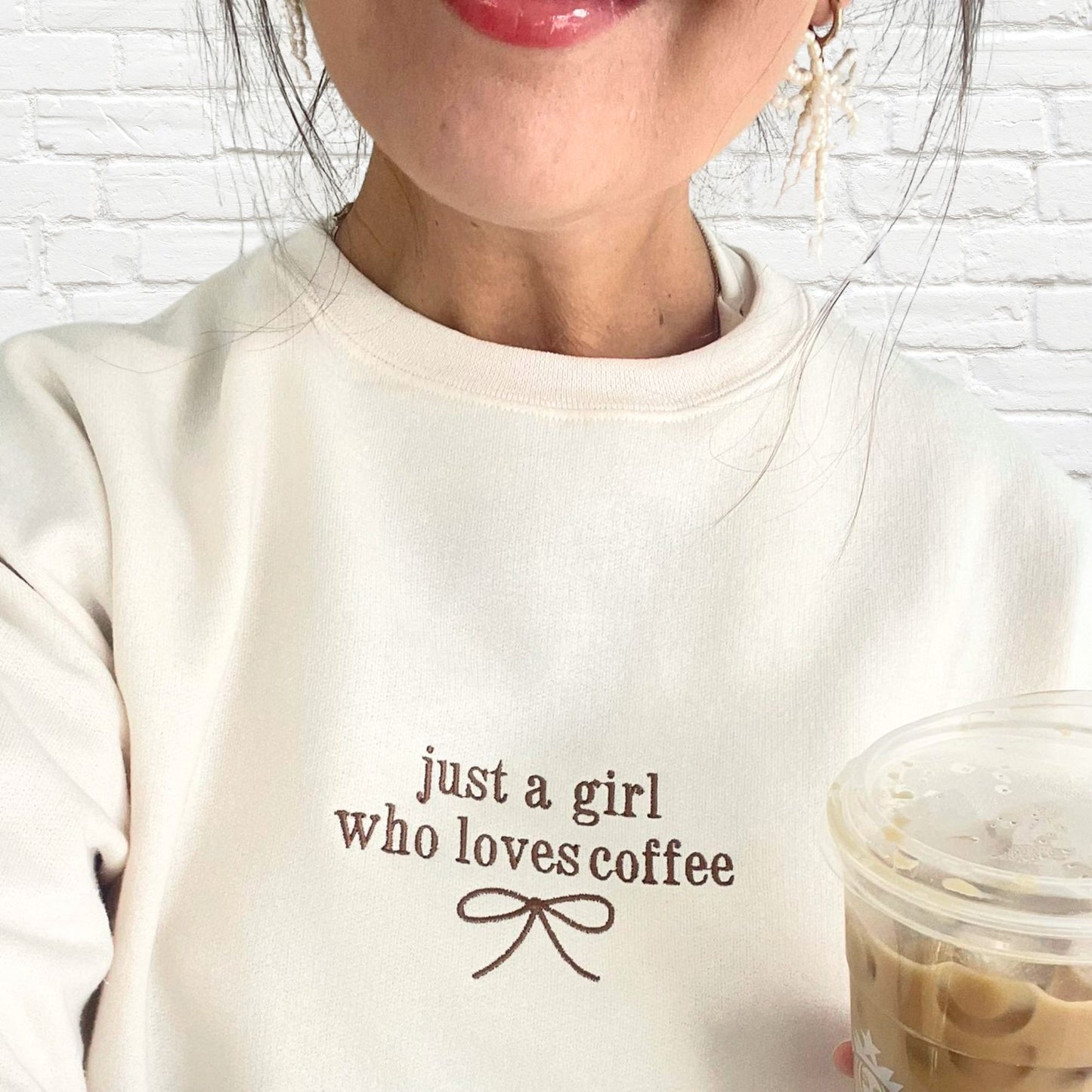 woman wearing a sweet cream crew with just a girl who loves coffee and a dainty bow embroidered on the center chest