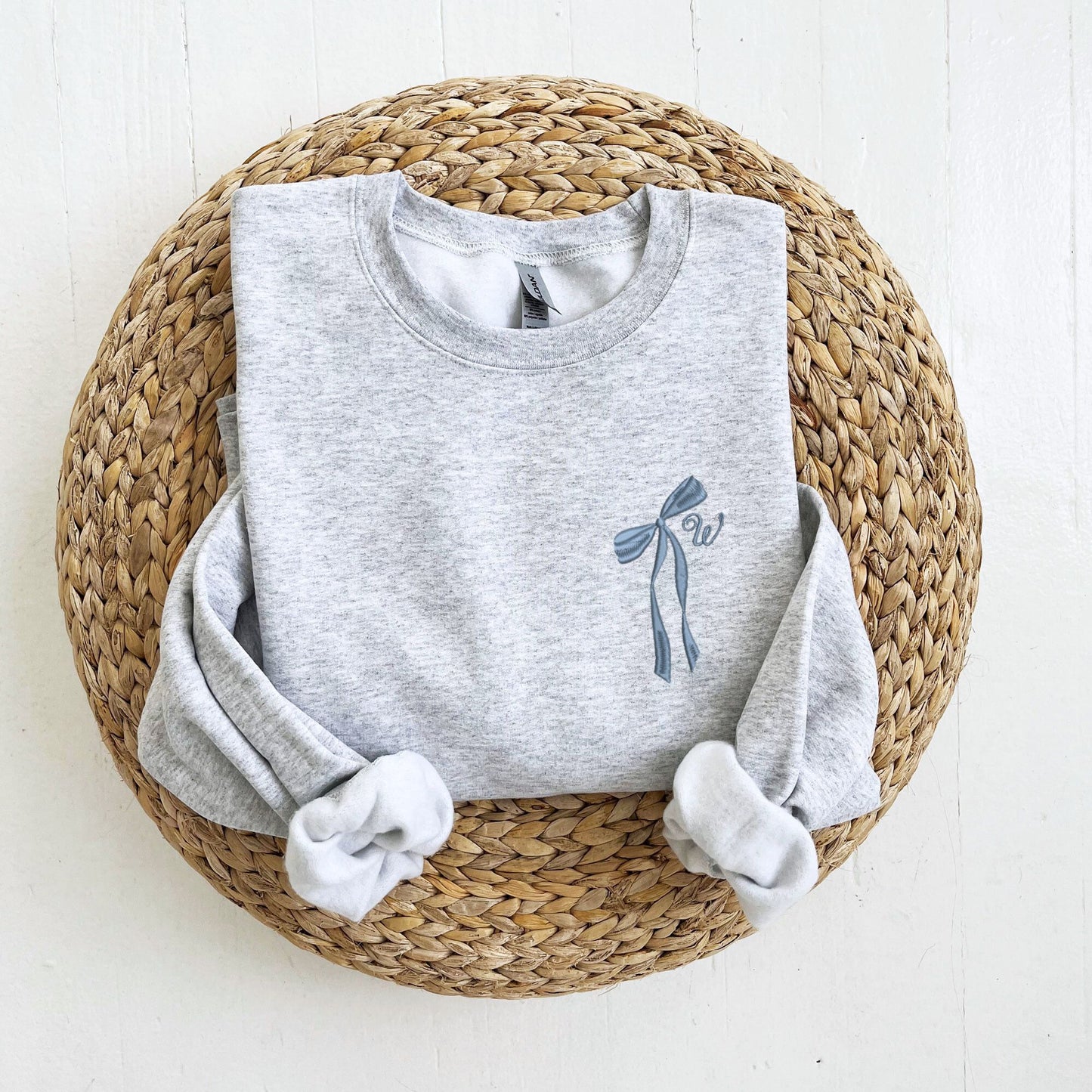 an ash sweatshirt with a ribbon bow and single initial embroidered design on the left chest in french blue thread