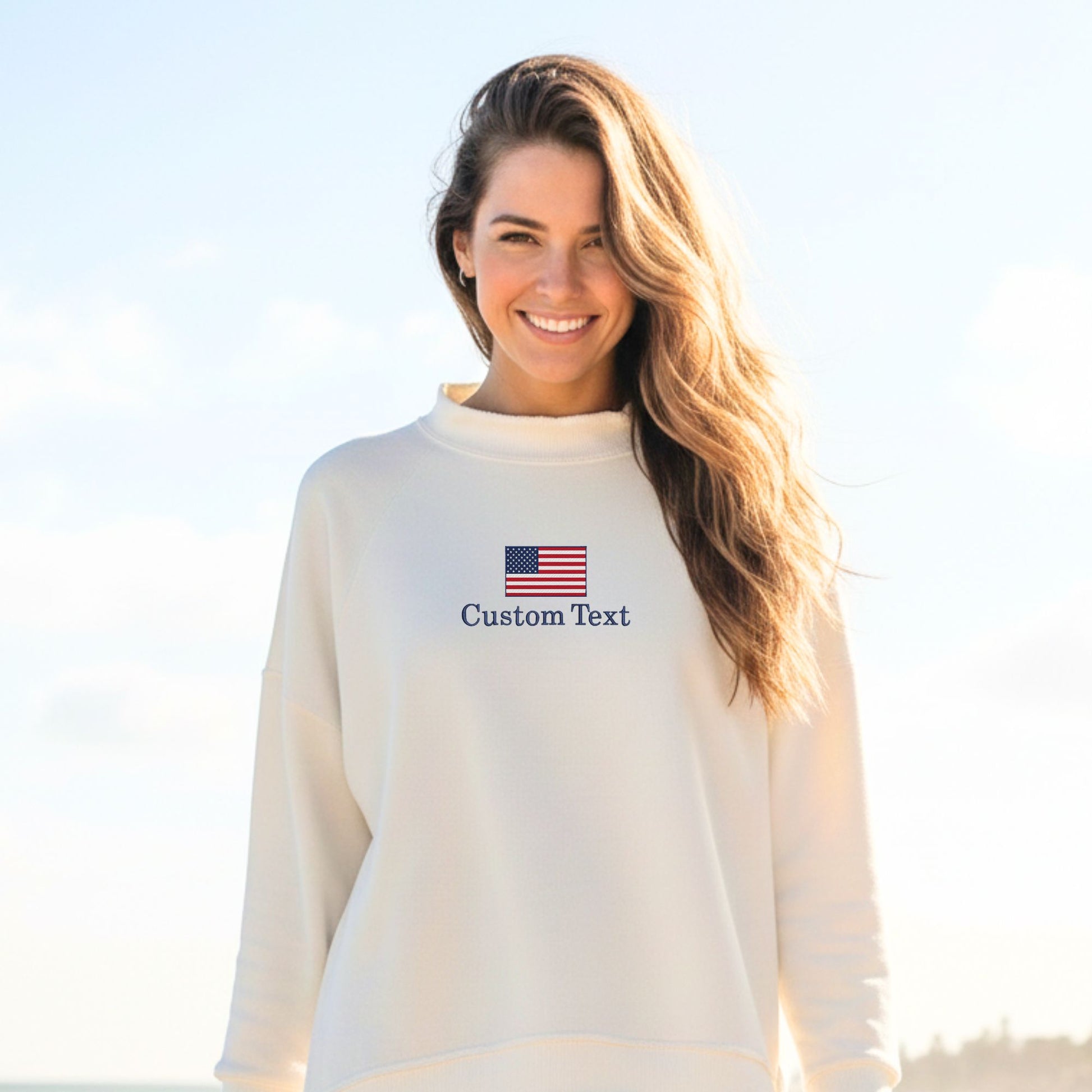 Woman wearing a white sweatshirt with an American flag and 'Custom Text' on a clear sky background