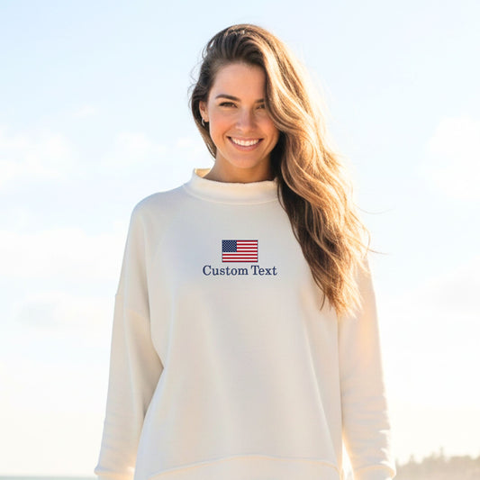 Woman wearing a white sweatshirt with an American flag and 'Custom Text' on a clear sky background