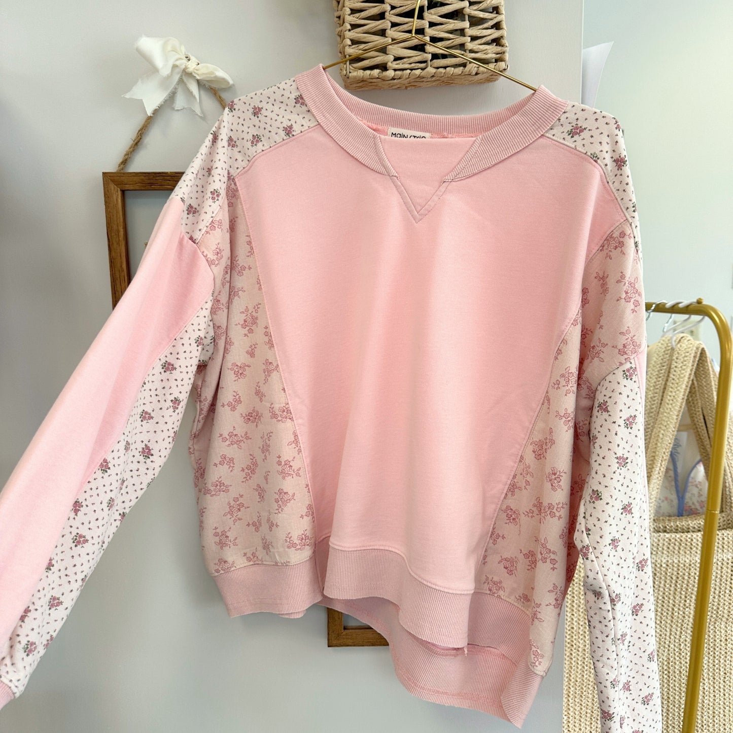 Pink sweatshirt with floral sleeves on a hanger against a neutral wall.