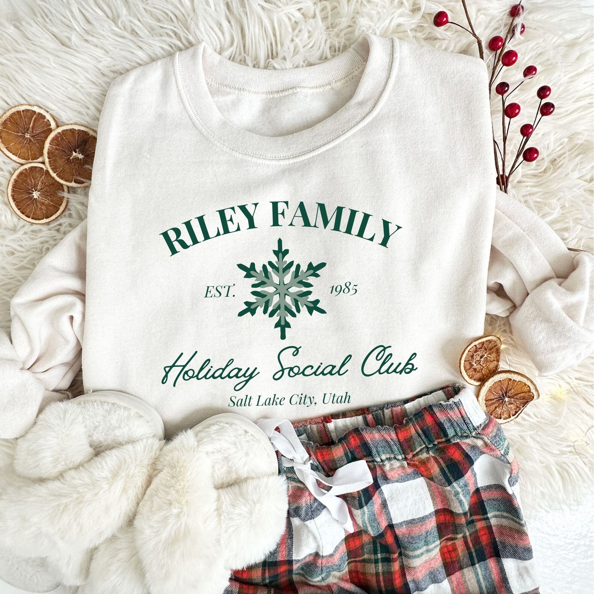 white crewneck sweatshirt with a custom print featuring a family name, Est date, snowflake, holiday social club, and location in green