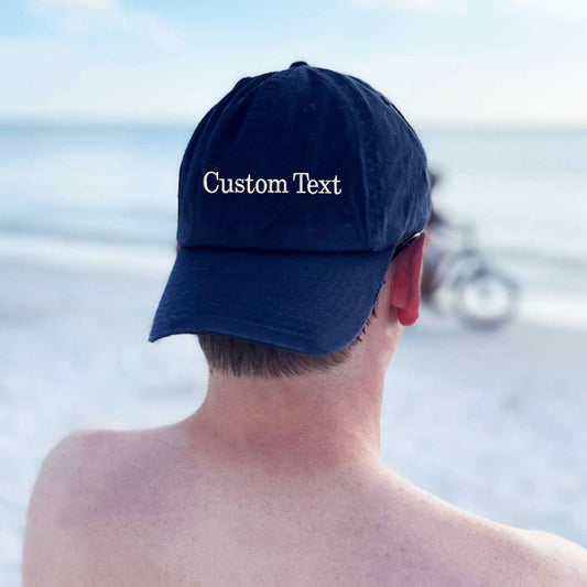 back view of a man on a beach wearing a navy hat with custom embroidered text in white thread