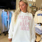 Woman wearing a white sweatshirt with 'Pilates is my happy hour' text in a store setting.