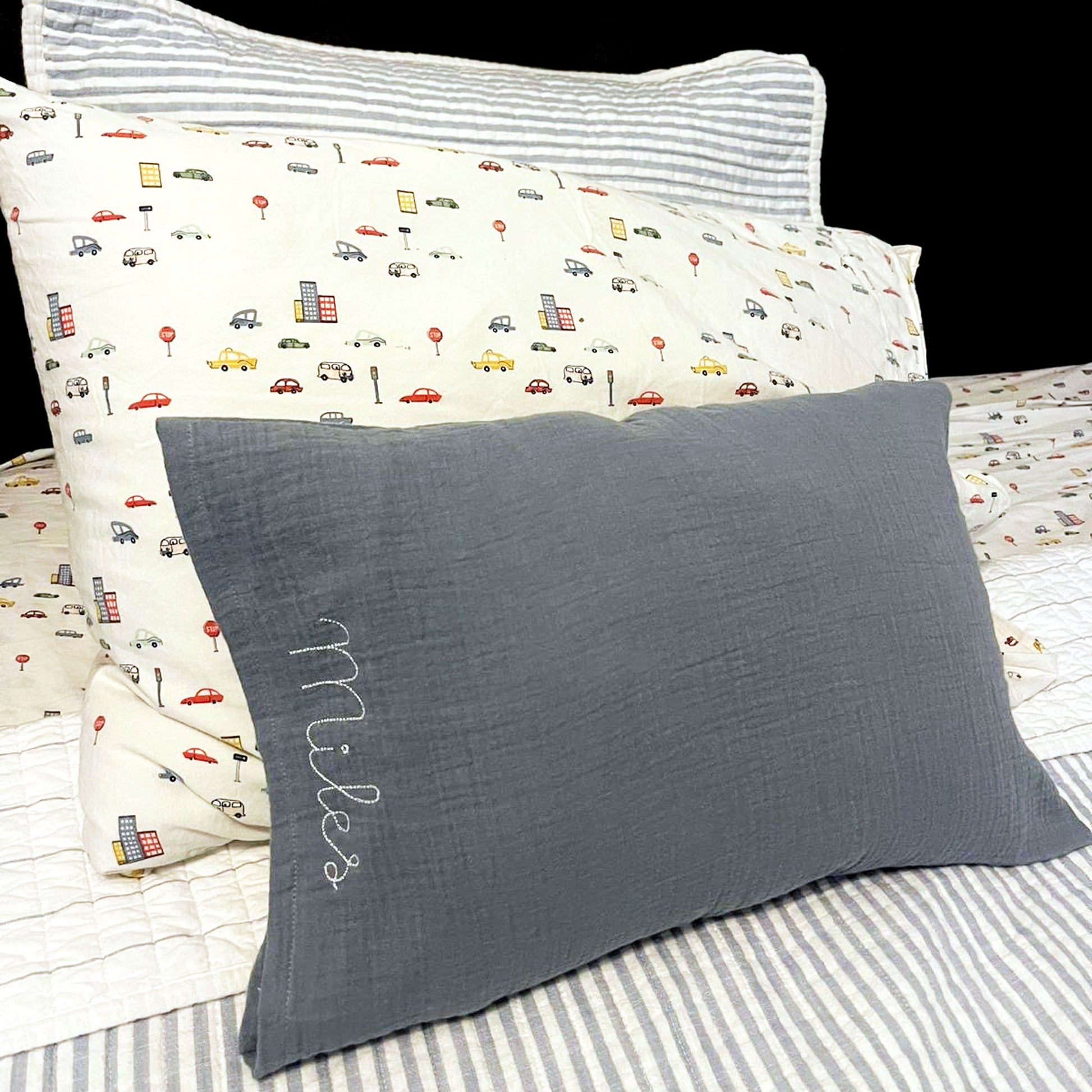 little boy's bed with a custom pillow with a muslin pillowcase and personalized name stitched embroidery along the side