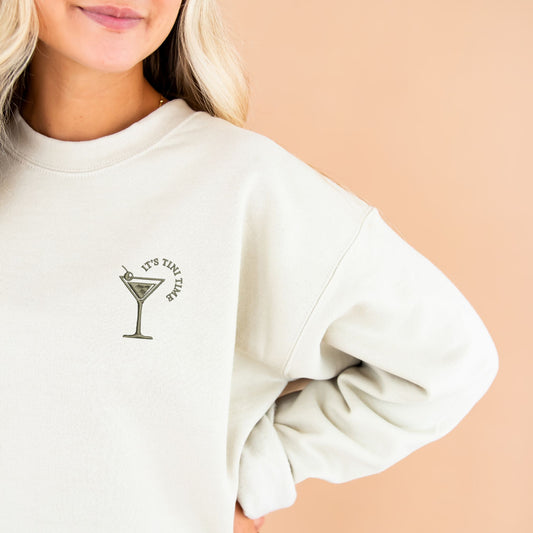 woman wearing a sand sweatshirt with custom martini tini time embroidered design on the left chest