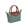 A small structured handbag in muted blue-green with brown leather handles, trim, and front flap detail, plus a gold-tone snap button and zipper hardware, shown on a plain white background.