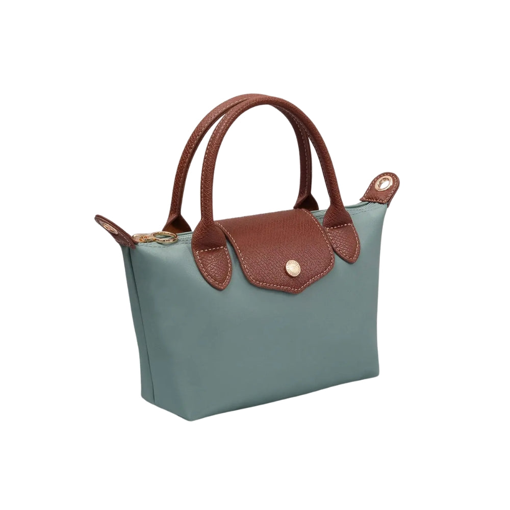 A small structured handbag in muted blue-green with brown leather handles, trim, and front flap detail, plus a gold-tone snap button and zipper hardware, shown on a plain white background.