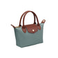 A small structured handbag in muted blue-green with brown leather handles, trim, and front flap detail, plus a gold-tone snap button and zipper hardware, shown on a plain white background.