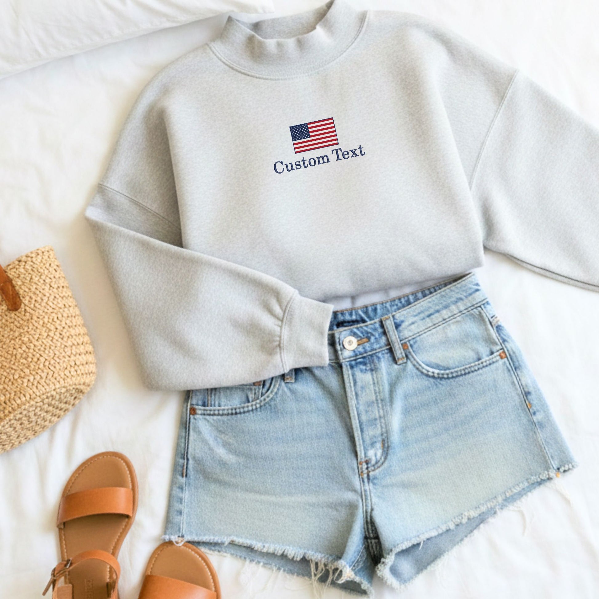 outfit layout featuring a gray mockneck sweatshirt with embroidered usa custom text design on the center chest paired with jean shorts and sandals 
