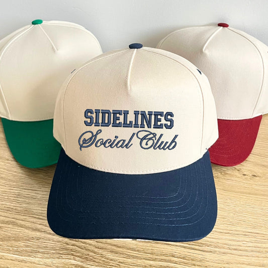 two tone canvas trucker hats in green, burgundy, and navy with a custom sidelines social club embroidered design