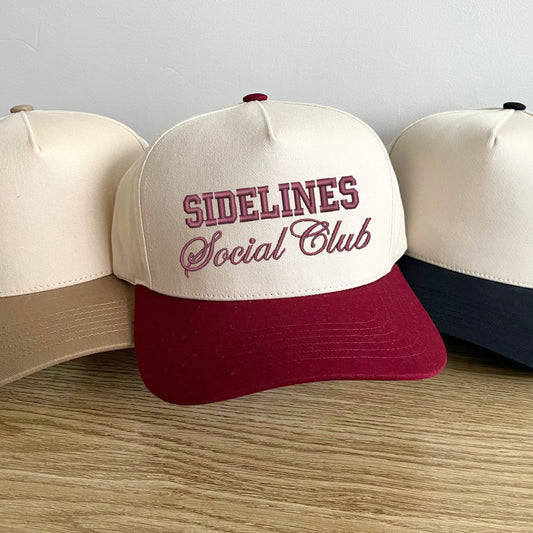 two tone canvas trucker hats in beige, burgundy, and black with a custom sidelines social club embroidered design