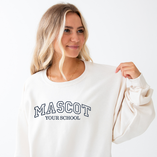 young woman wearing a sweet cream crewneck sweatshirt with custom embroidered athletic block text for mascot and school name  