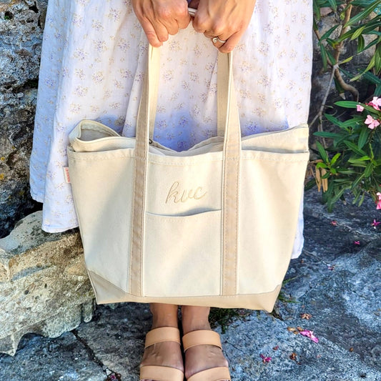 woman holding a medium boat tote with safari trim with font 5 embroidered monogram, a script font, embroidered above the front pocket in camel thread