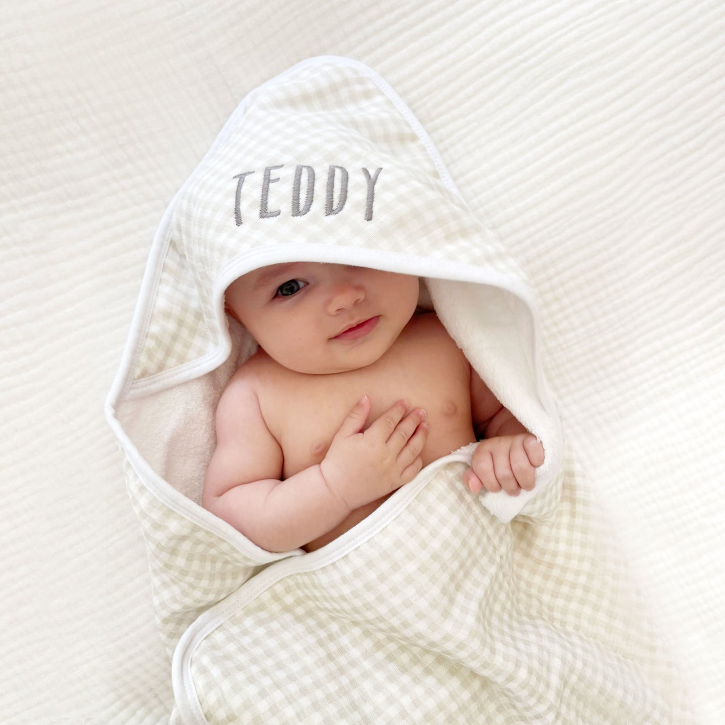 baby wrapped in a tan plaid hooded bath towel with name embroidered on the hood in a dark gray thread