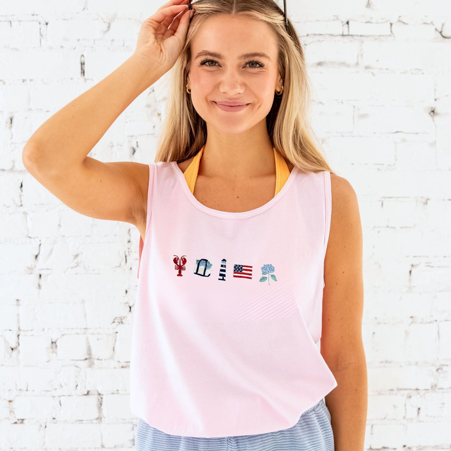Woman wearing a pink tank top with colorful designs against a white brick wall.