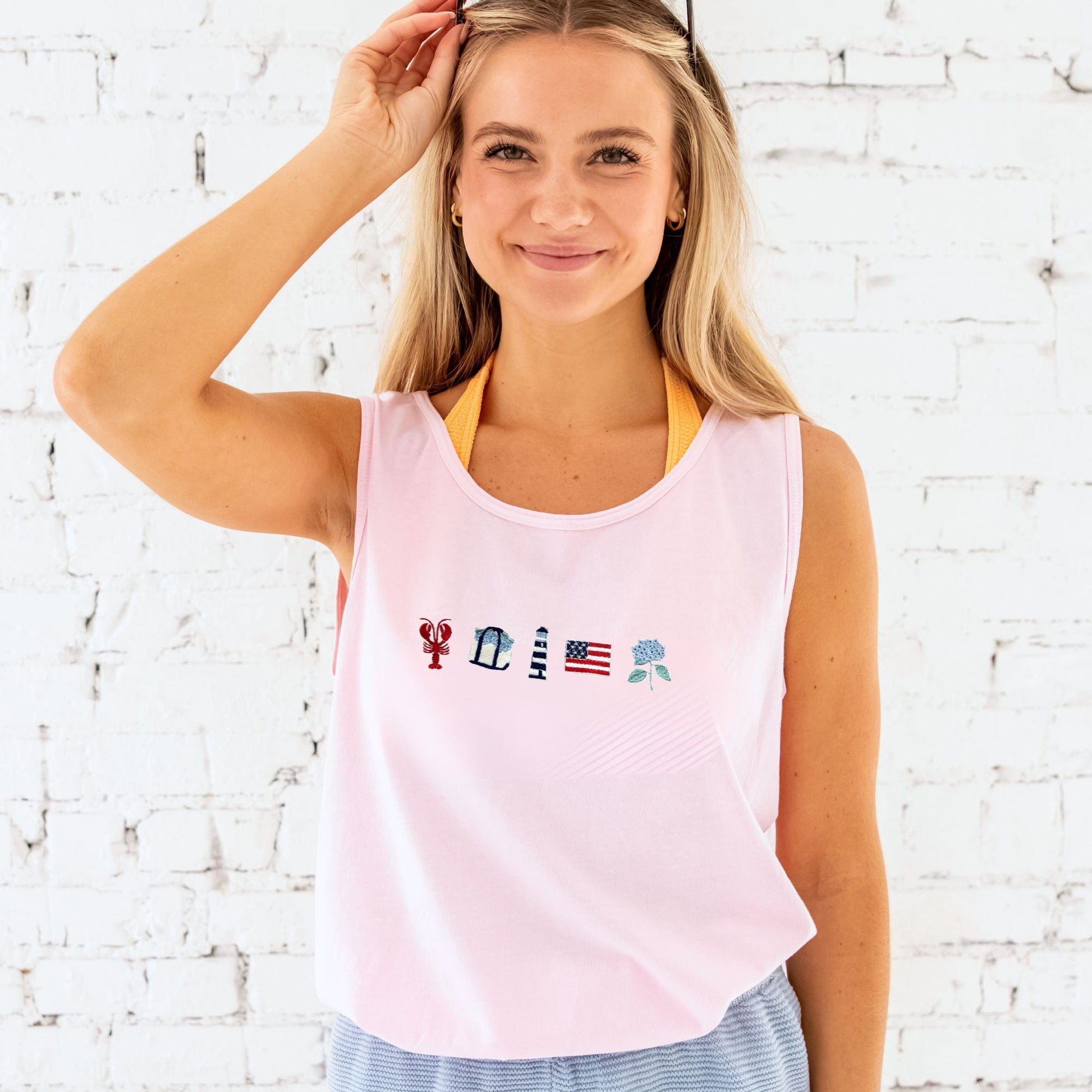Woman wearing a pink tank top with colorful designs against a white brick wall.