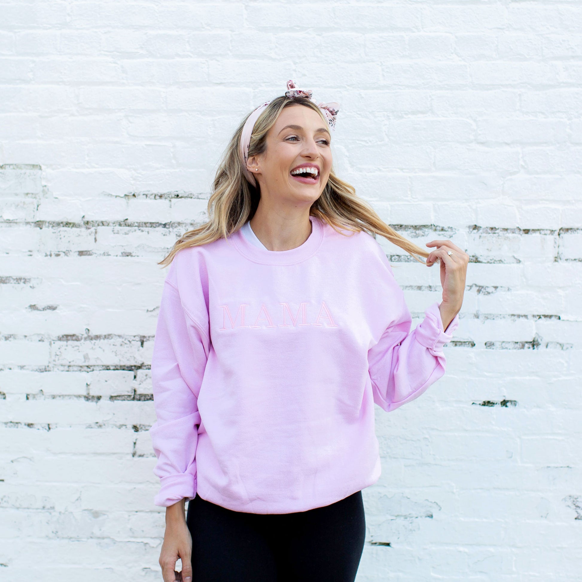 young woman modeling a light pink crewneck sweatshirt with embroidered MAMA in all caps and in baby pink thread across the chest