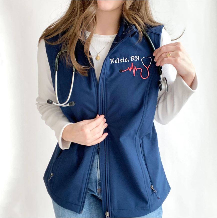 young woman wearing a blue soft shell vest with embroidered nurse stethoscope and name on the left chest