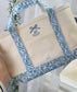 Beige tote bag with blue floral handles and 'elle' embroidery on a white background