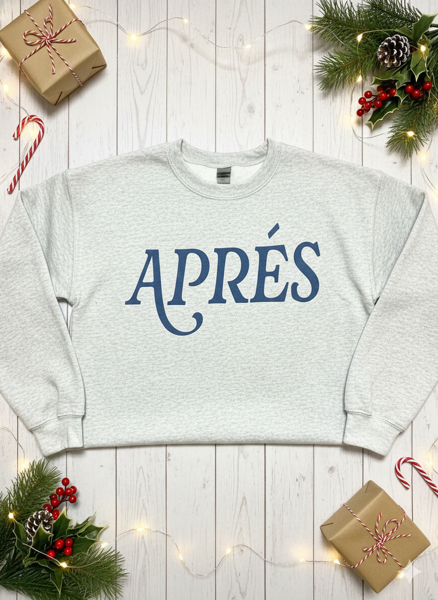 Gray sweatshirt with 'APRéS' text on a wooden surface with Christmas decorations.