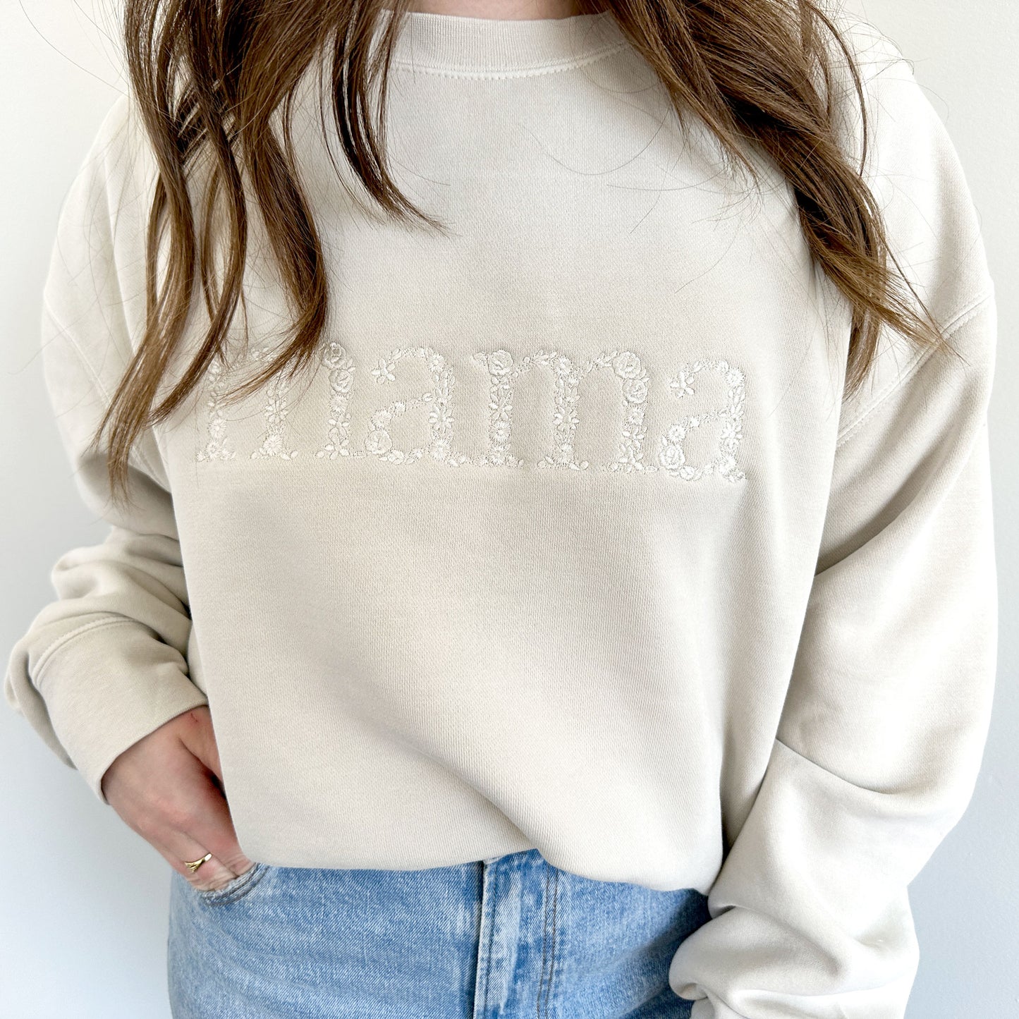 close up of woman wearing an oversized cream pullover sweatshirt with mama embroidered in lower case letters in a floral font