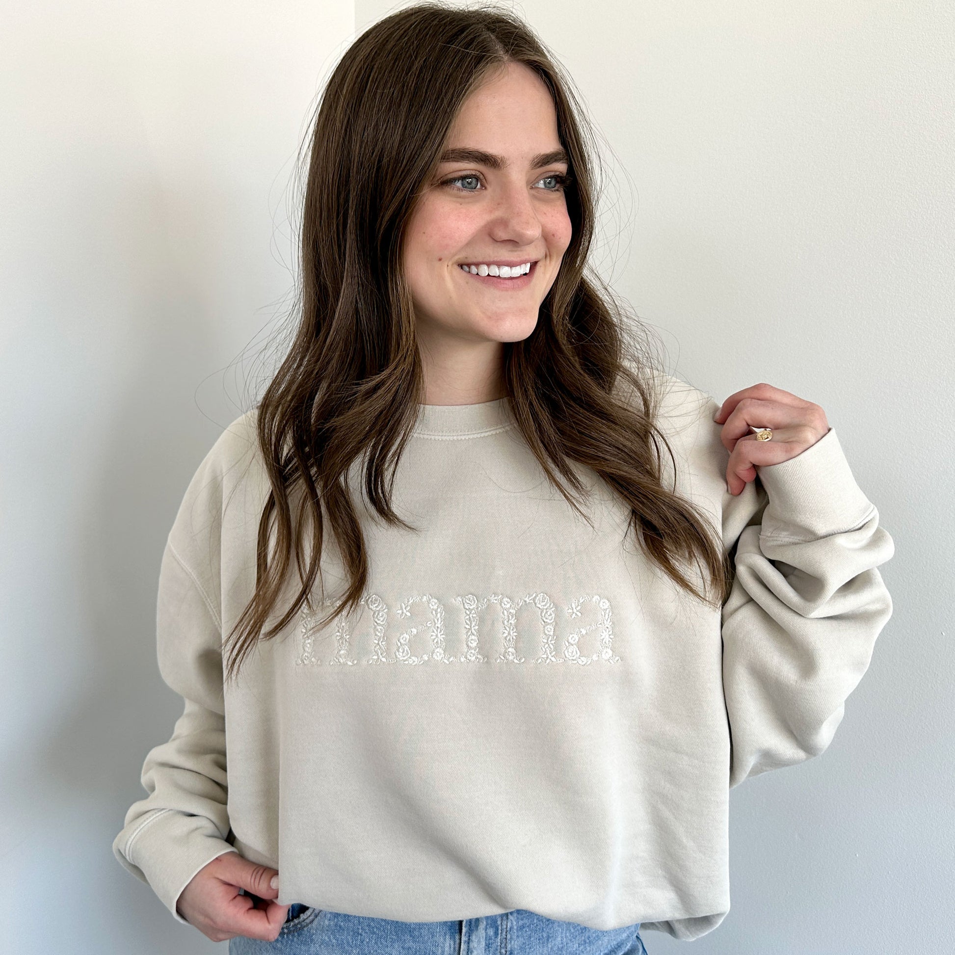 woman wearing an ivory pullover oversized sweatshirt with mama embroidered in a floral font acorss the chest